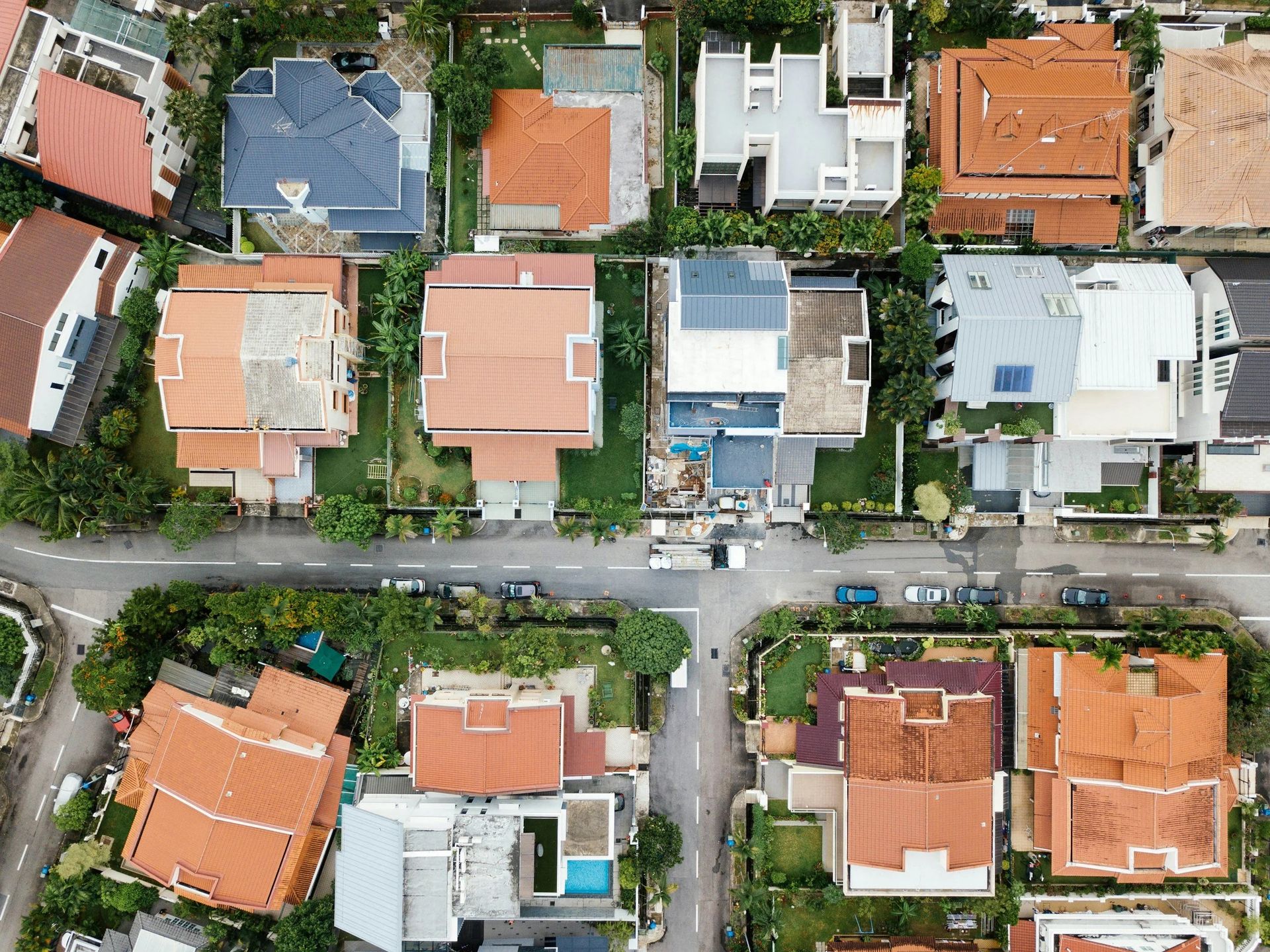 Aerial view of a suburban neighborhood with houses, roads, and trees. Roofs are various colors.
