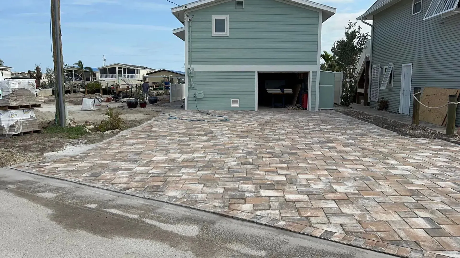 Brick driveway leading to a teal house with a garage, beside another house.