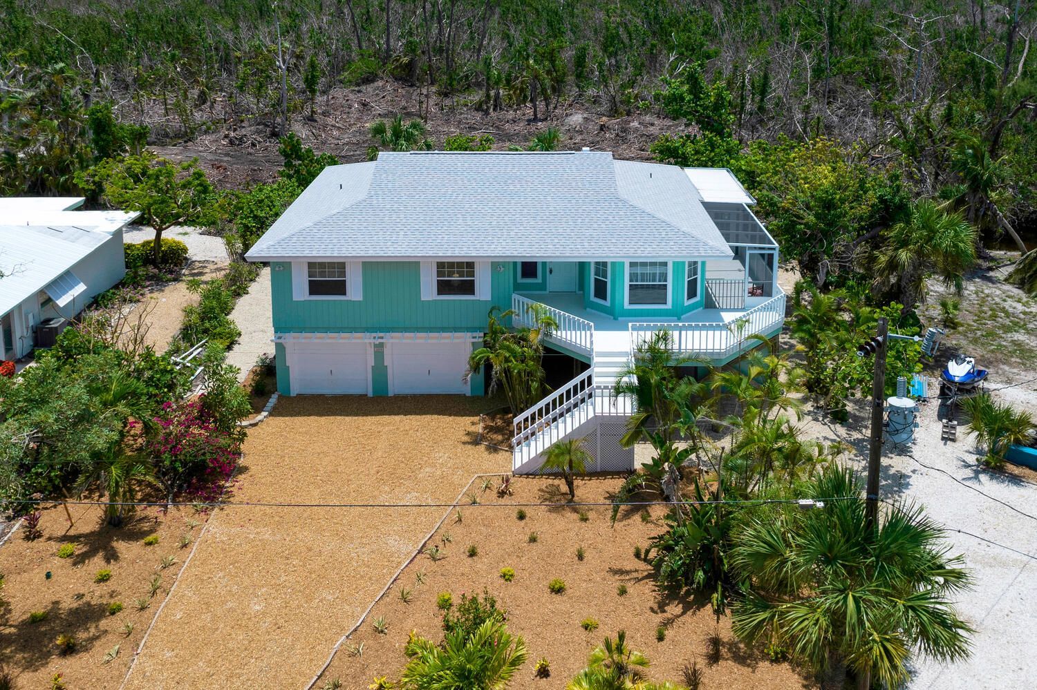 Blue and white beach house with a gravel driveway and surrounding foliage.