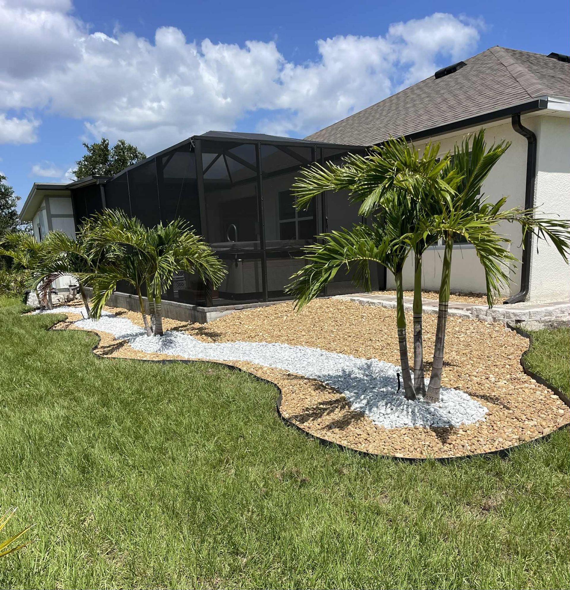 A landscaped backyard with palm trees, beige gravel, white rocks, and a screened-in porch.