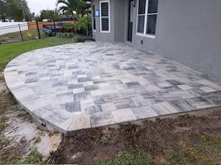 Curved patio paved with gray pavers next to a gray house with green grass.