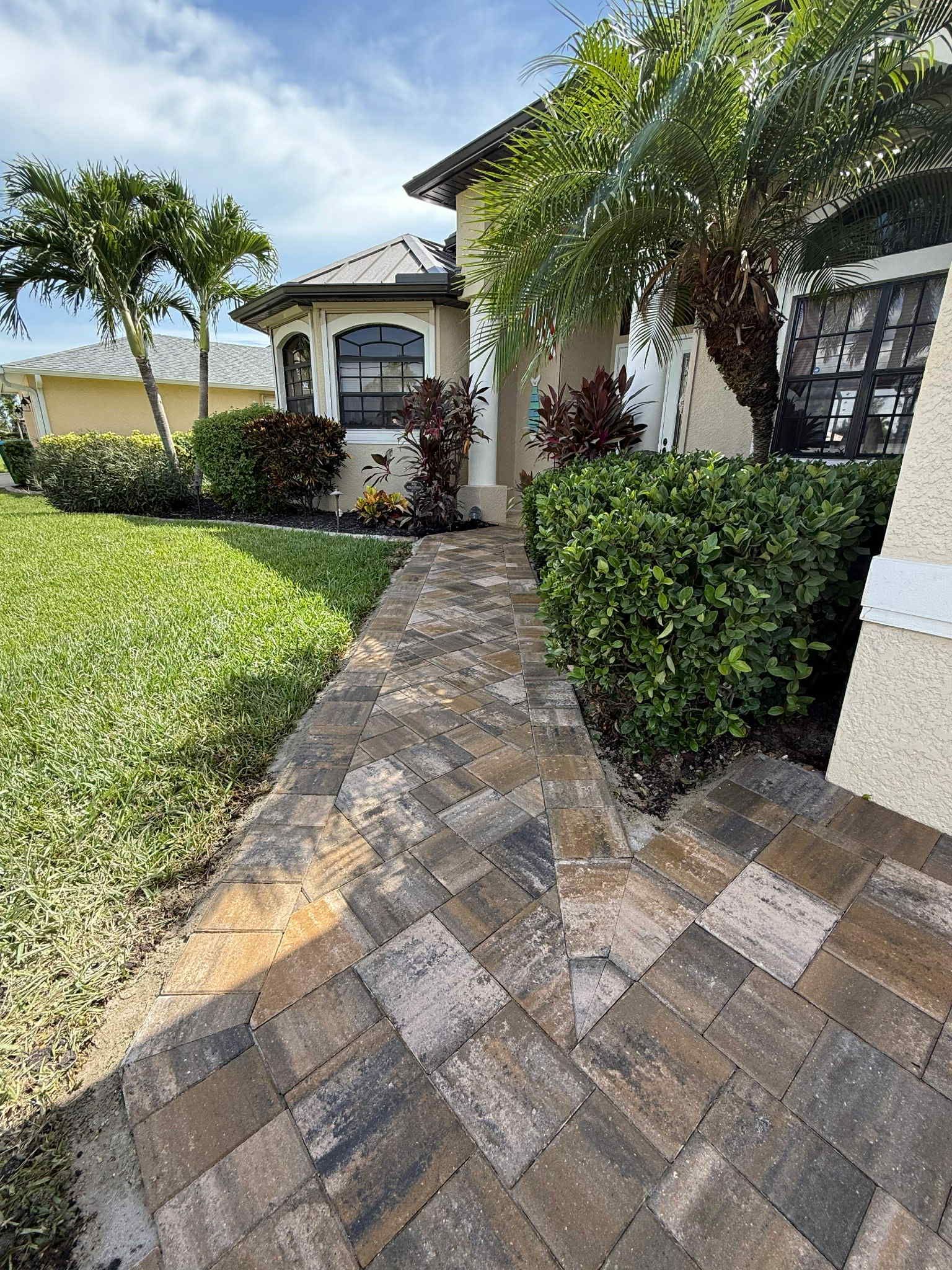 Stone walkway leading to a light-colored house with landscaping; blue sky overhead.