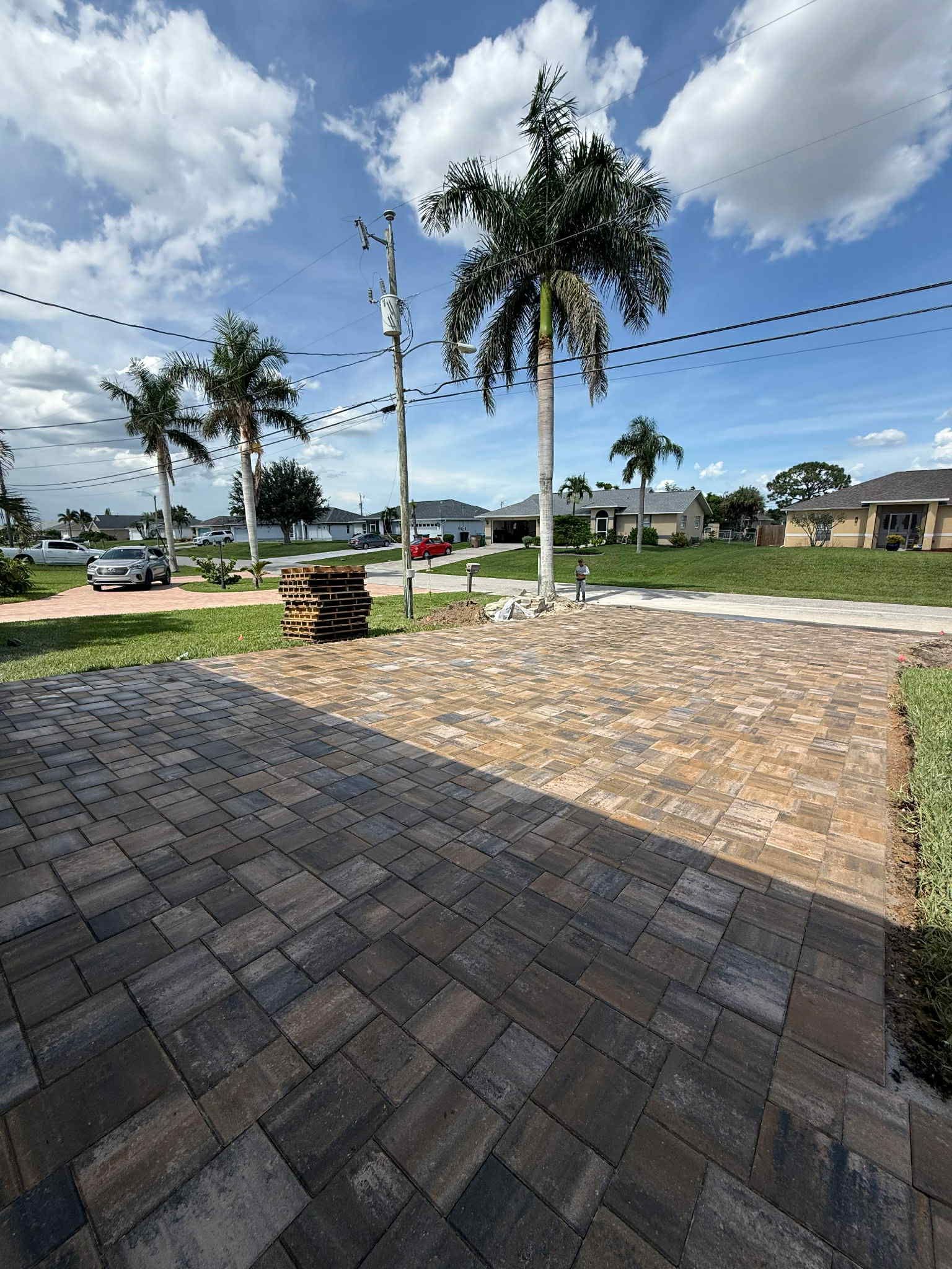 Brick patio in front of a street with palm trees and houses under a cloudy sky.