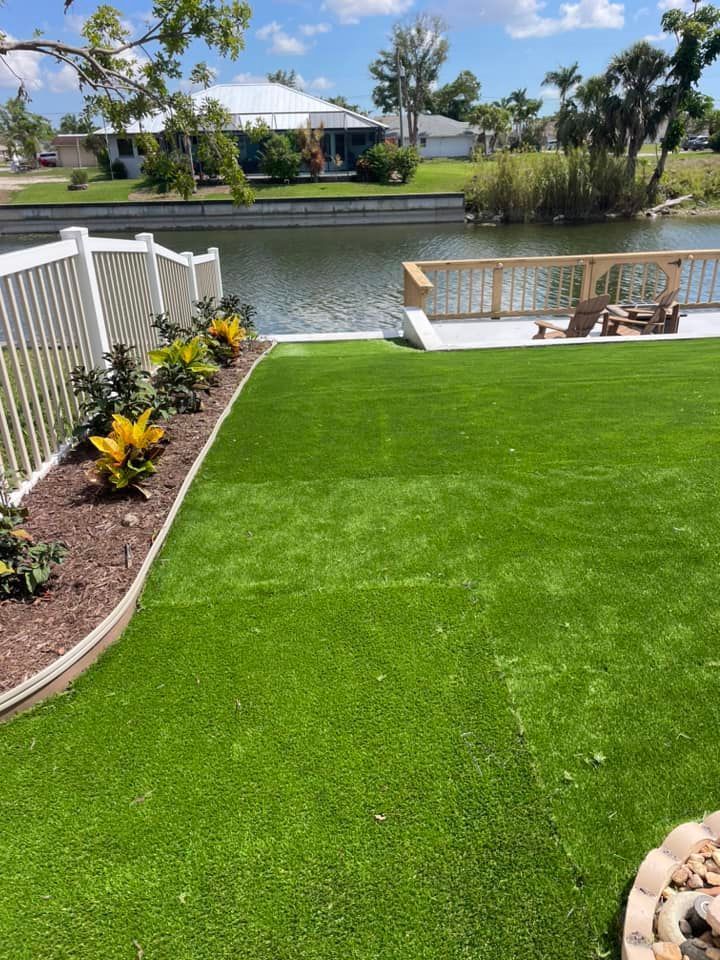 Green turf yard next to a waterway, a white fence, and a wooden deck.