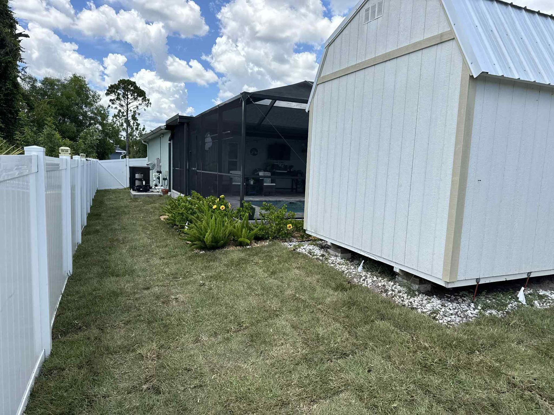 A white fence and shed border a grassy yard with a screened pool enclosure.