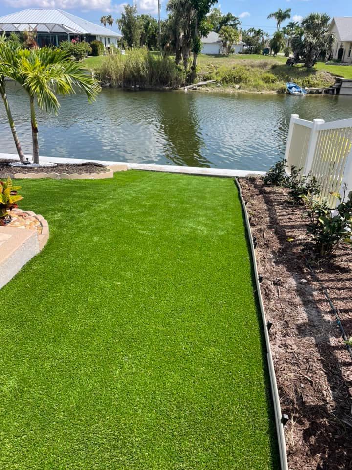 Lush green artificial turf lawn next to a canal with a white fence and palm trees.