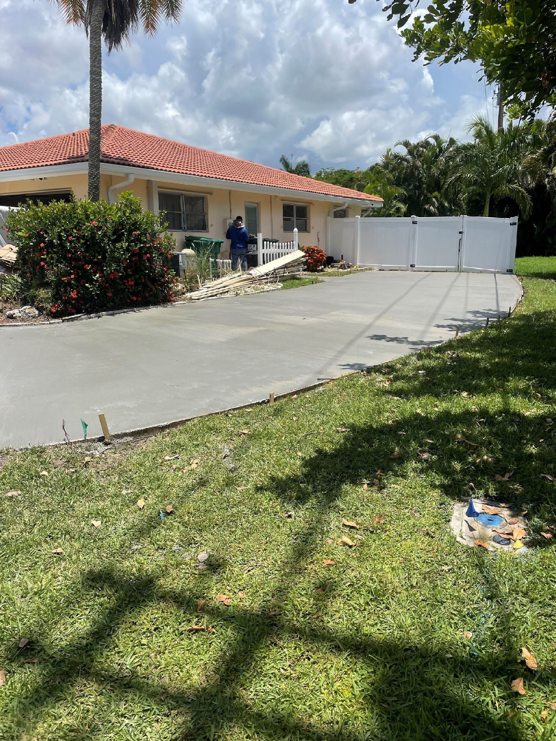 House with red tile roof and white fence, man working in the yard with concrete driveway and green grass.