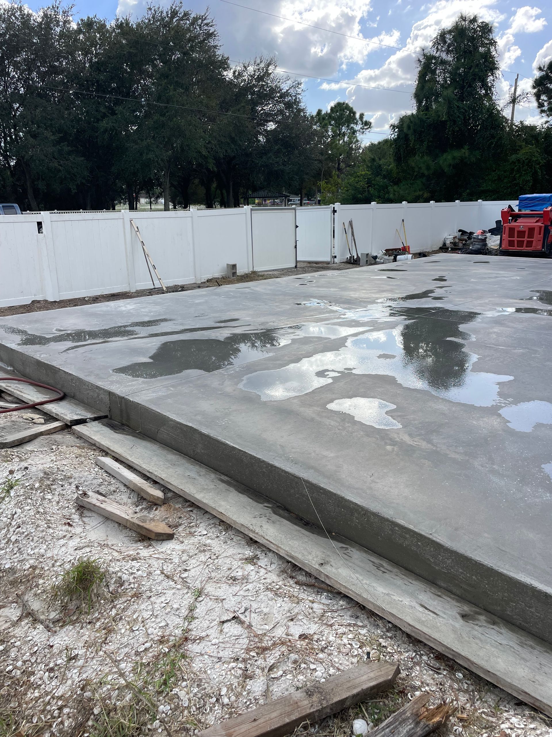 Newly poured concrete slab with a white fence in the background. Construction site outdoors.