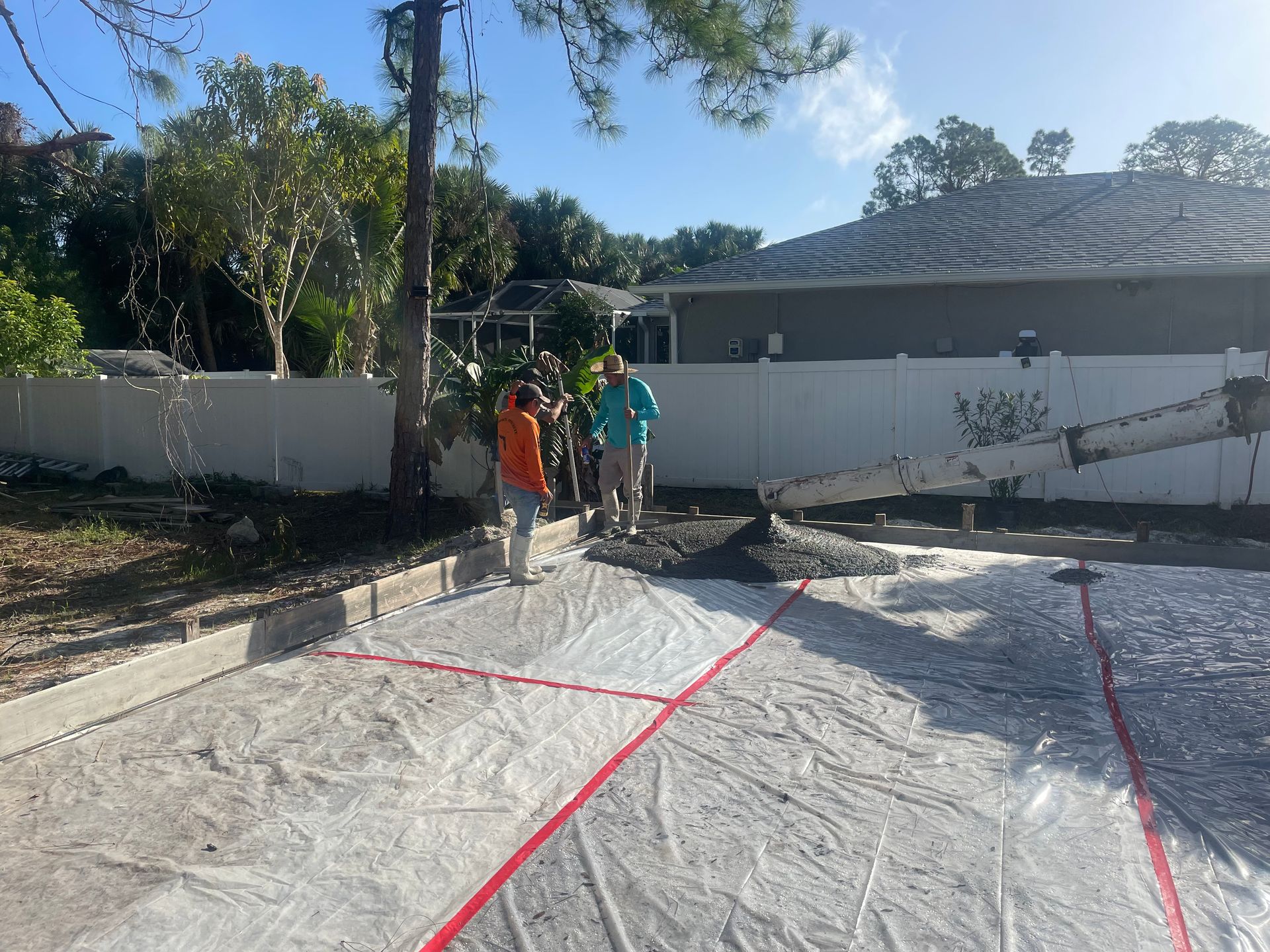 Two workers pouring concrete, sunny outdoor setting. Red lines mark sections.