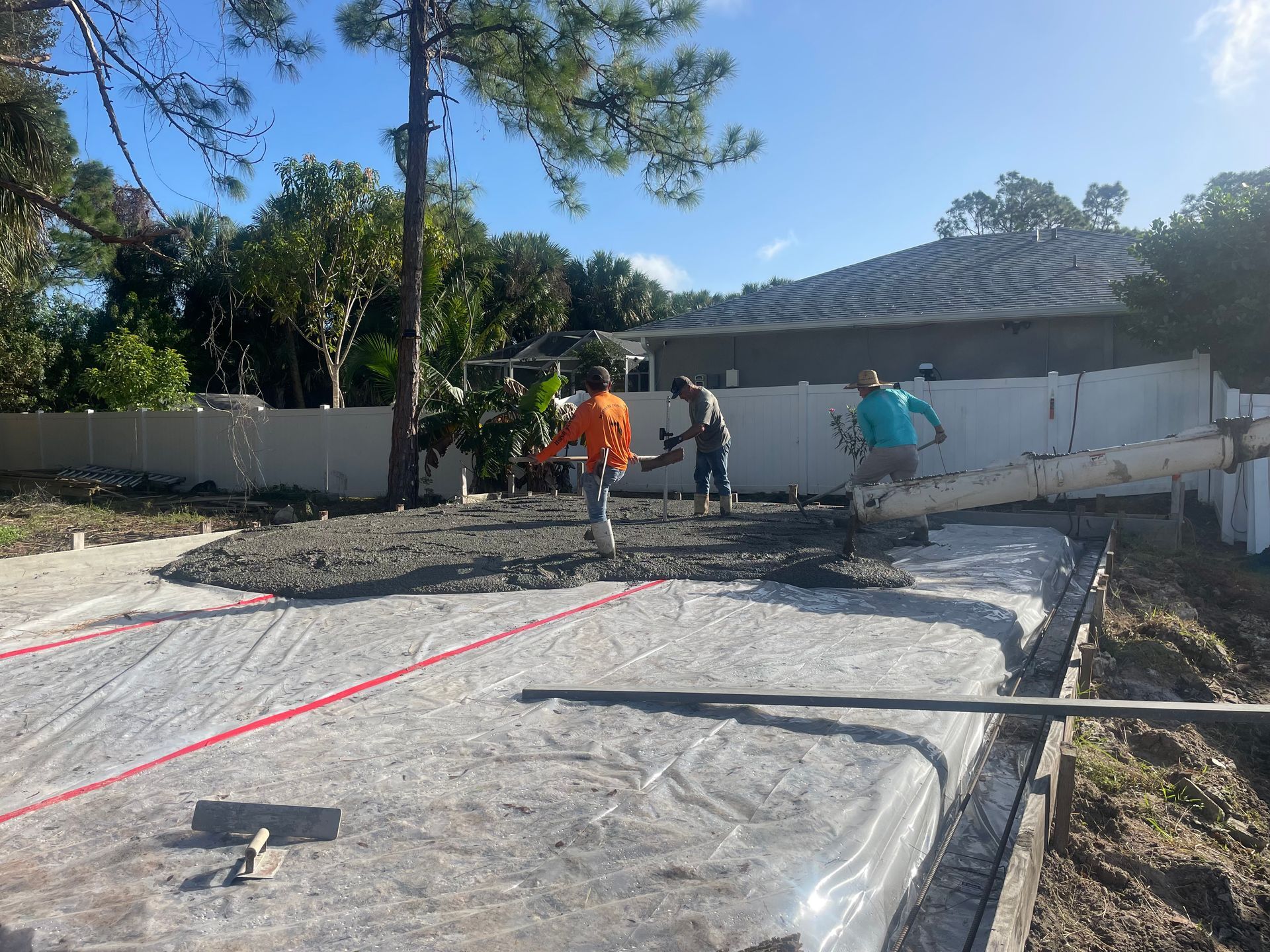 Construction workers pouring concrete into a form; orange vests, sunny outdoor setting.