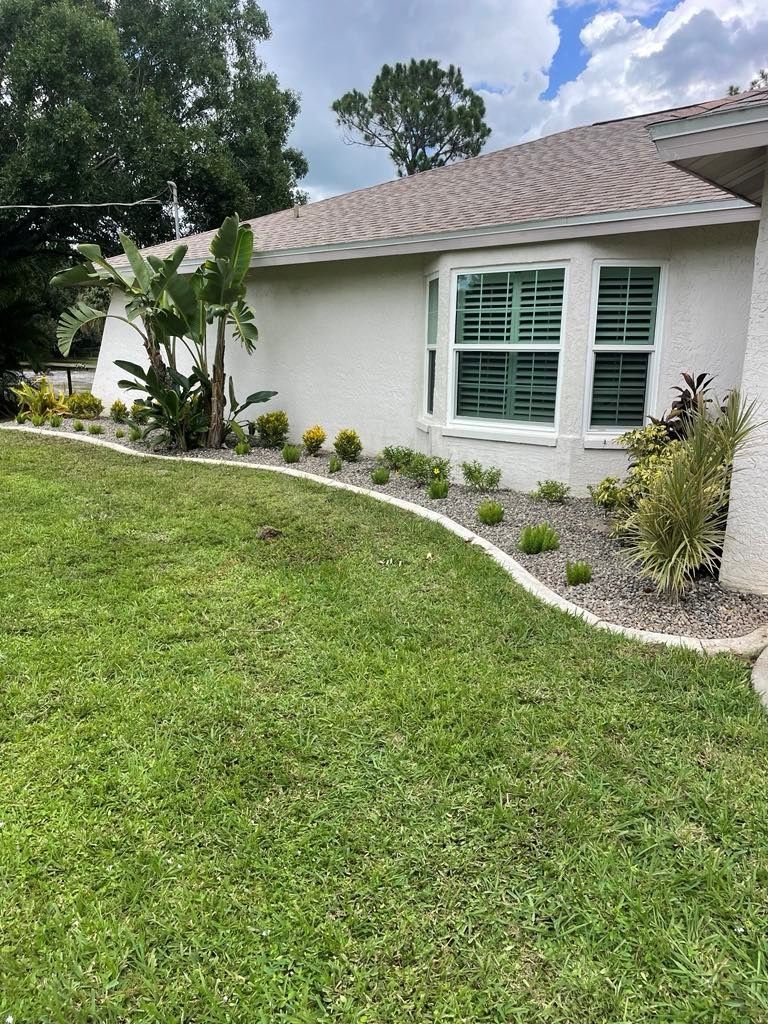 A well-manicured lawn with a curved flowerbed in front of a house with a bay window.
