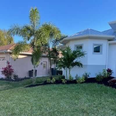 House with palm trees in front of a green lawn, blue sky overhead.
