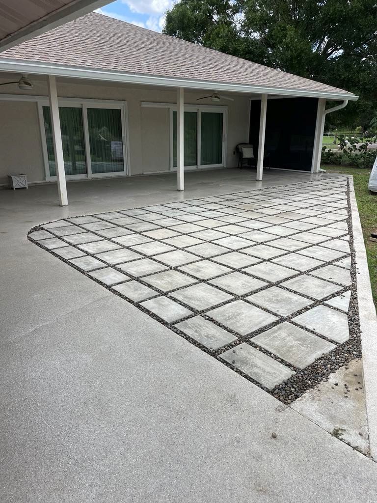 Concrete patio with gray pavers and dark pebbles leading to a house with sliding glass doors.