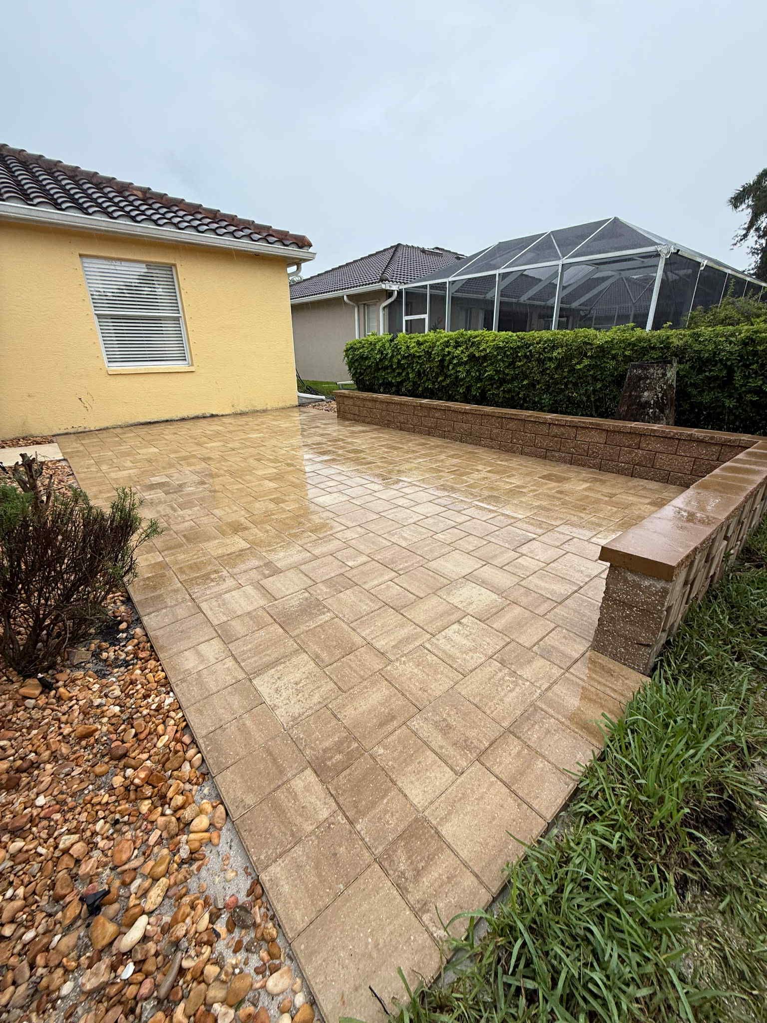 Brick patio with low brick walls, tan and brown, with a yellow house and greenery visible.