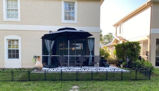 Backyard patio with black gazebo, furniture, and black and white patterned flooring, surrounded by a black fence.