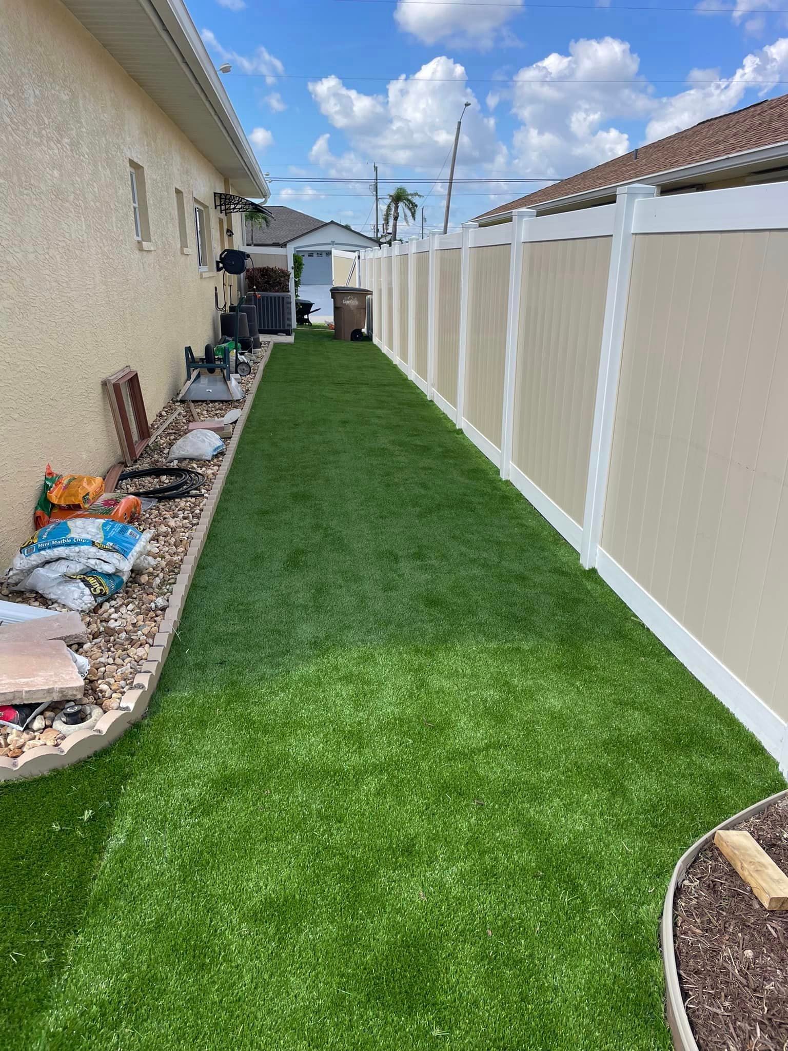 Narrow backyard with artificial turf, tan fence, and beige stucco wall, sunny day.