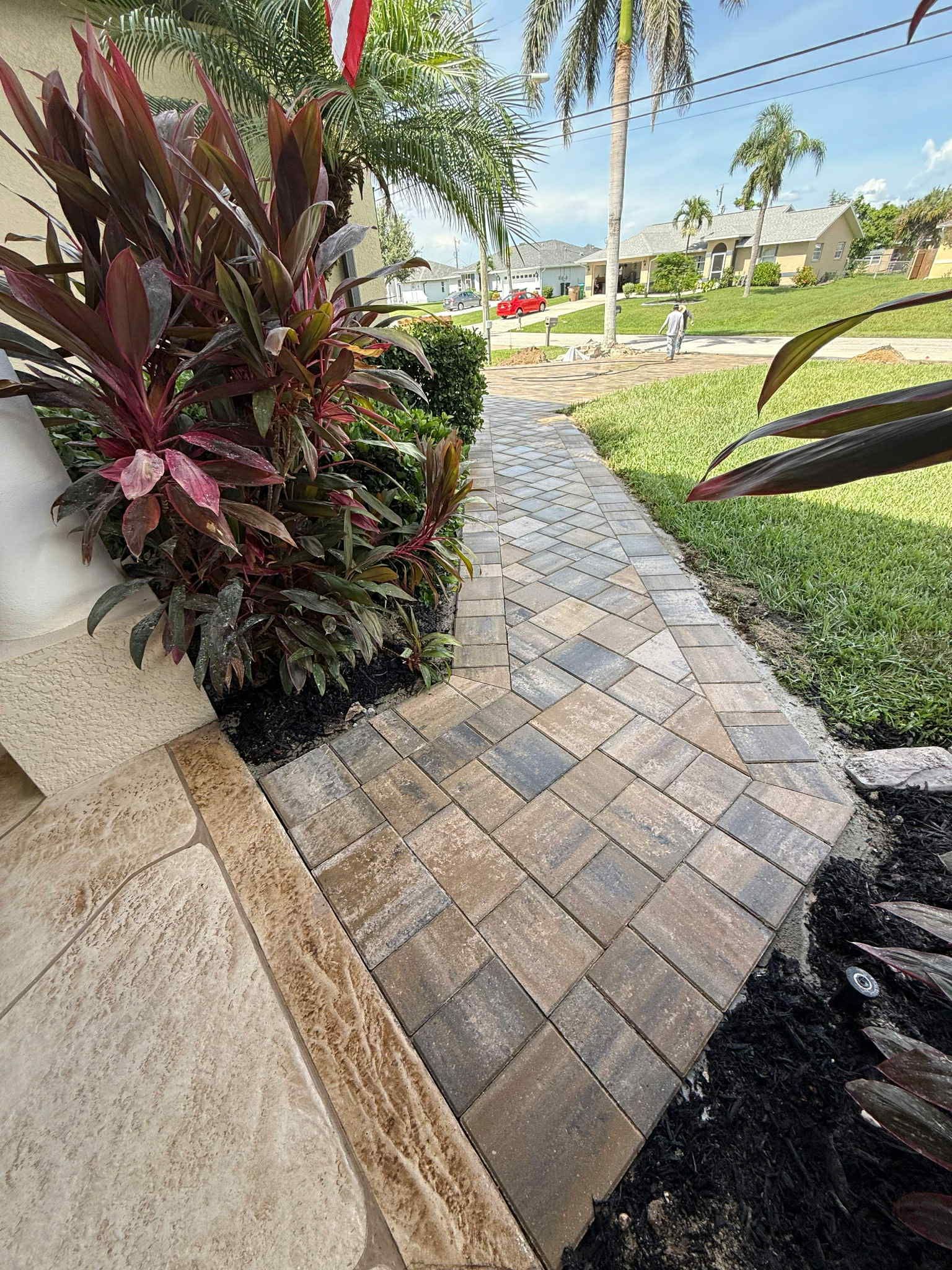 Brick pathway leading from a house to a street, bordered by landscaping.