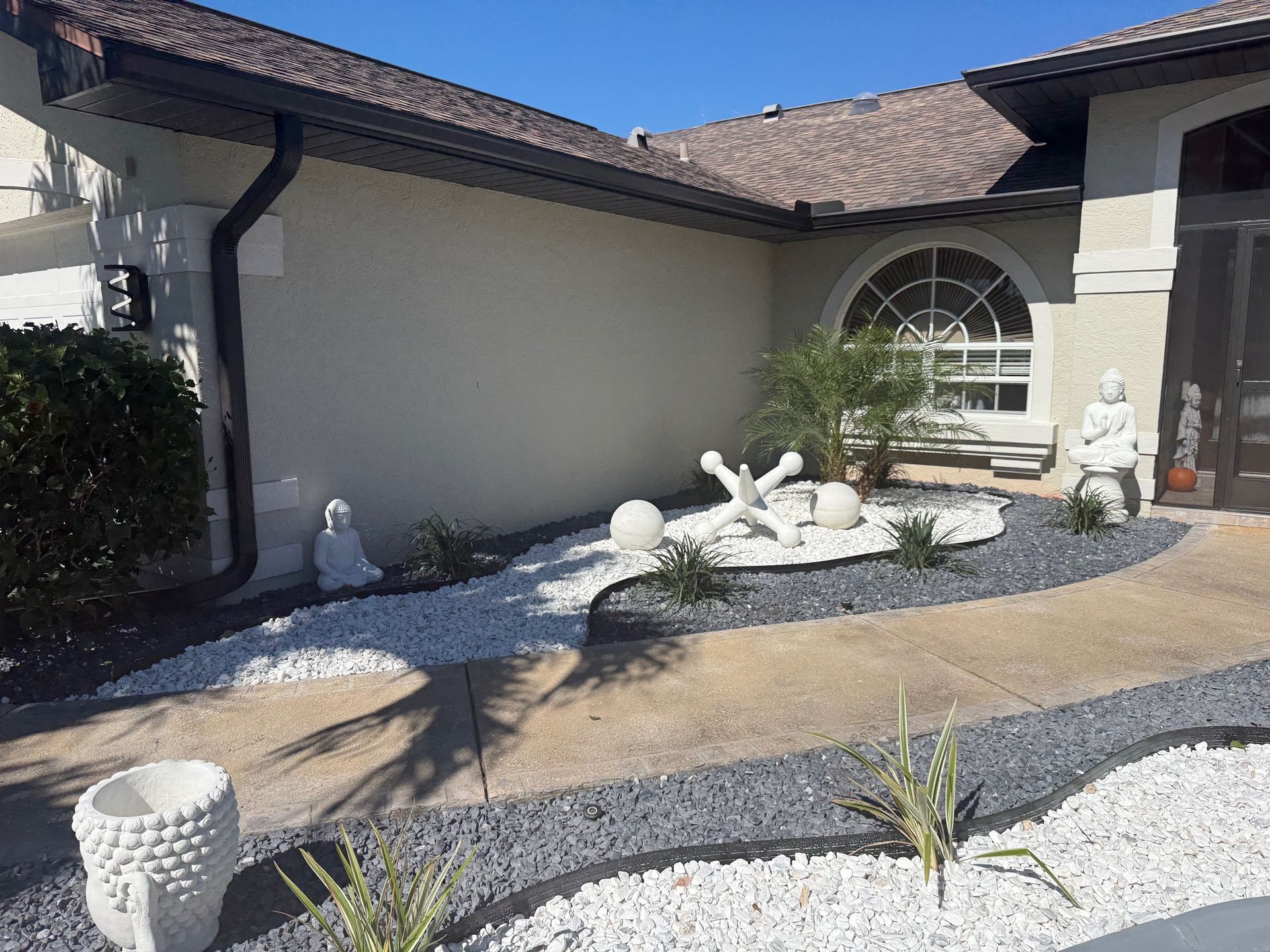 Exterior view of a house with a landscaped garden bed featuring white and gray gravel, sculptures, and small plants.