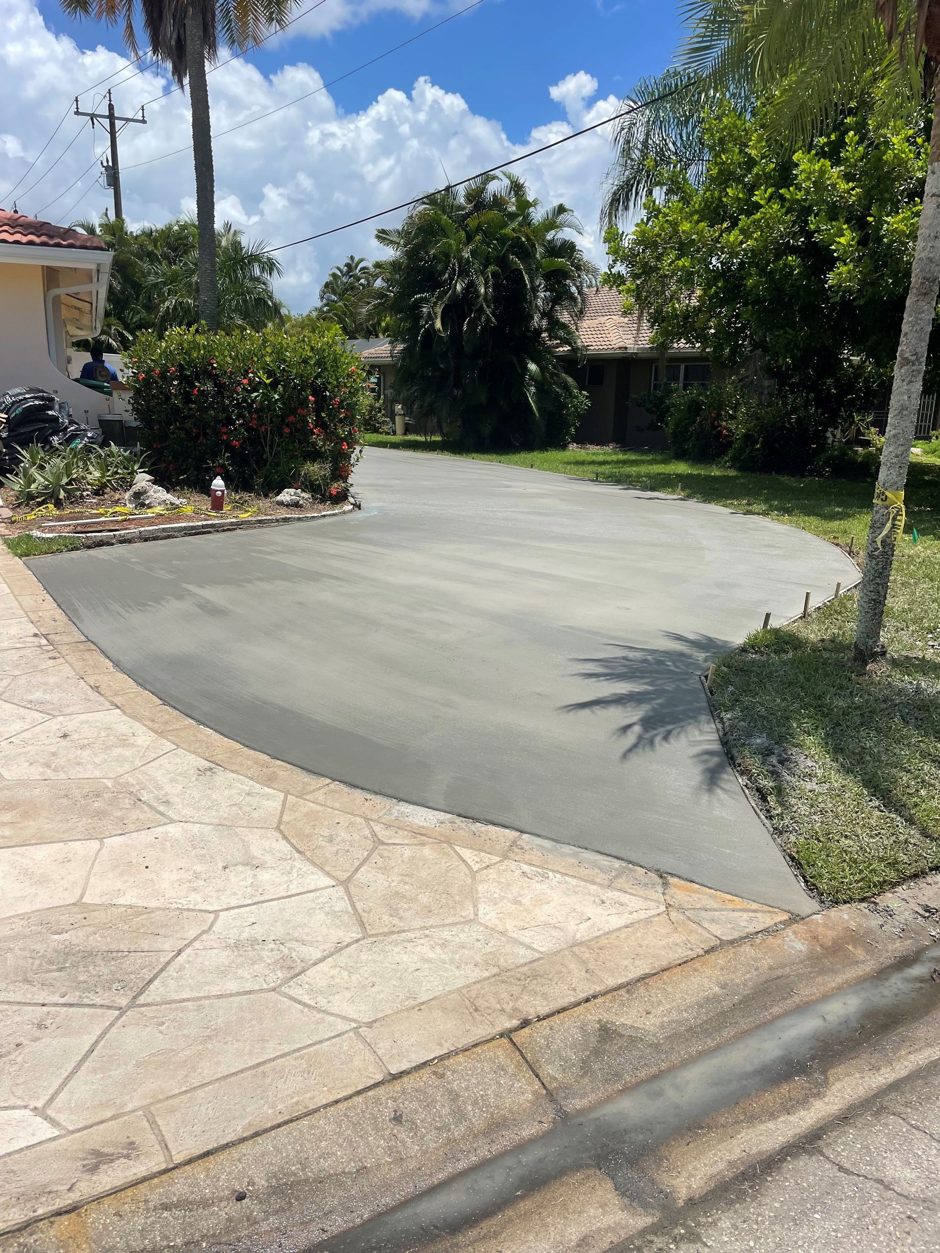Asphalt driveway curving from stamped concrete, flanked by greenery, sunny day.