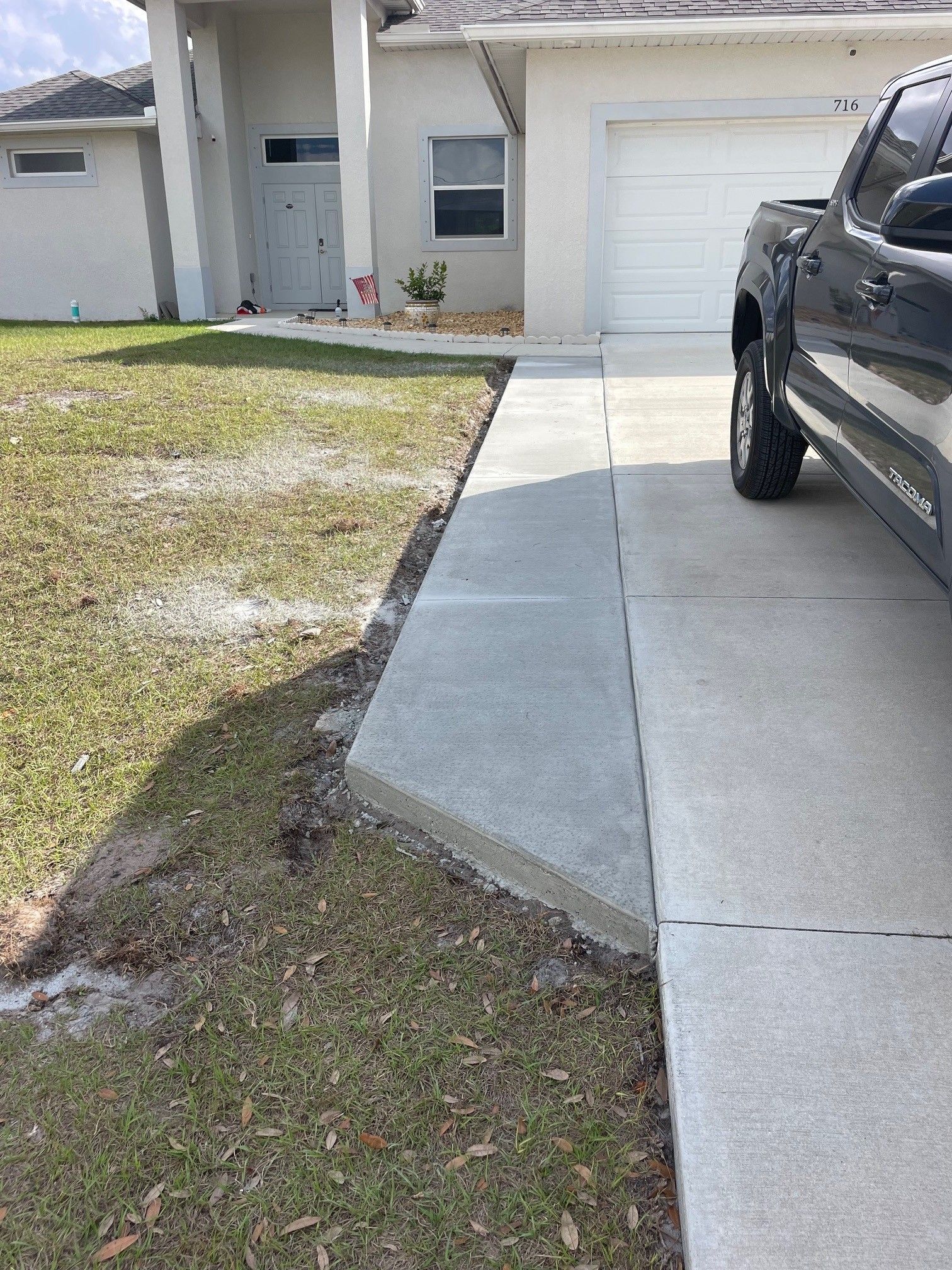 A concrete walkway extension leading to a residential front door next to a driveway with a parked truck.