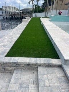Green turf strip between stone pathways near a pool and waterfront.