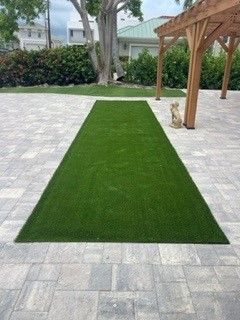A rectangular patch of green turf on a gray paver patio; wooden pergola in background.