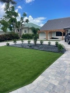 Green lawn with landscaping, driveway, and a house under a blue sky.