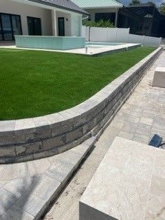 Curved stone retaining wall bordering artificial green lawn in a modern outdoor setting.
