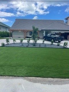 A house with green lawn and blue stone border, a truck parked in garage under a blue sky.