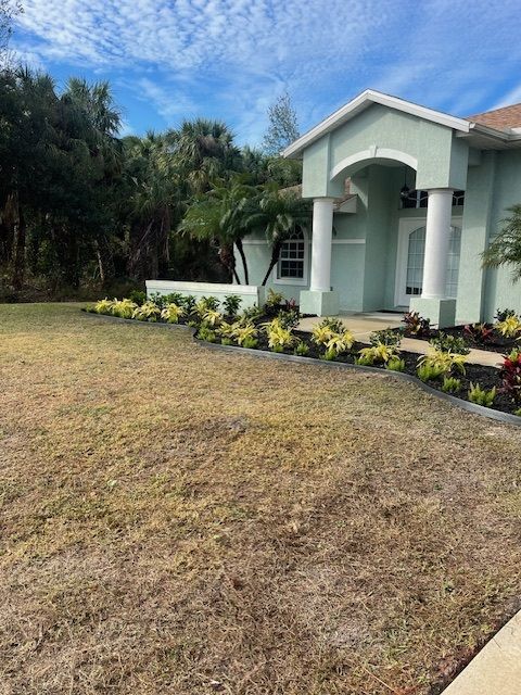 A light green house with a manicured lawn and landscaping on a sunny day.