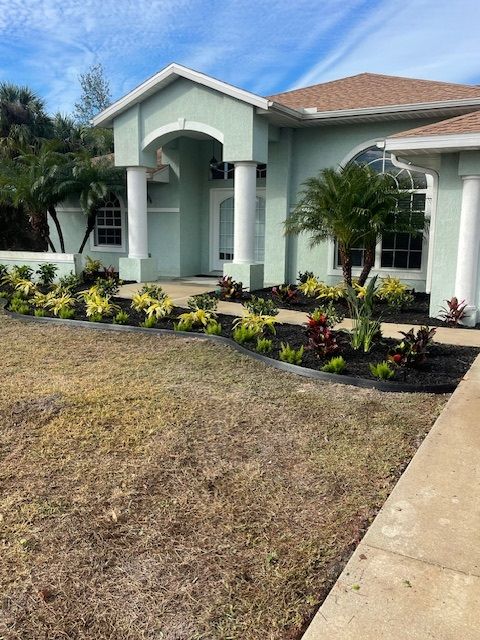 House with aqua exterior, white columns, and landscaped flower beds with a brown lawn in the foreground.