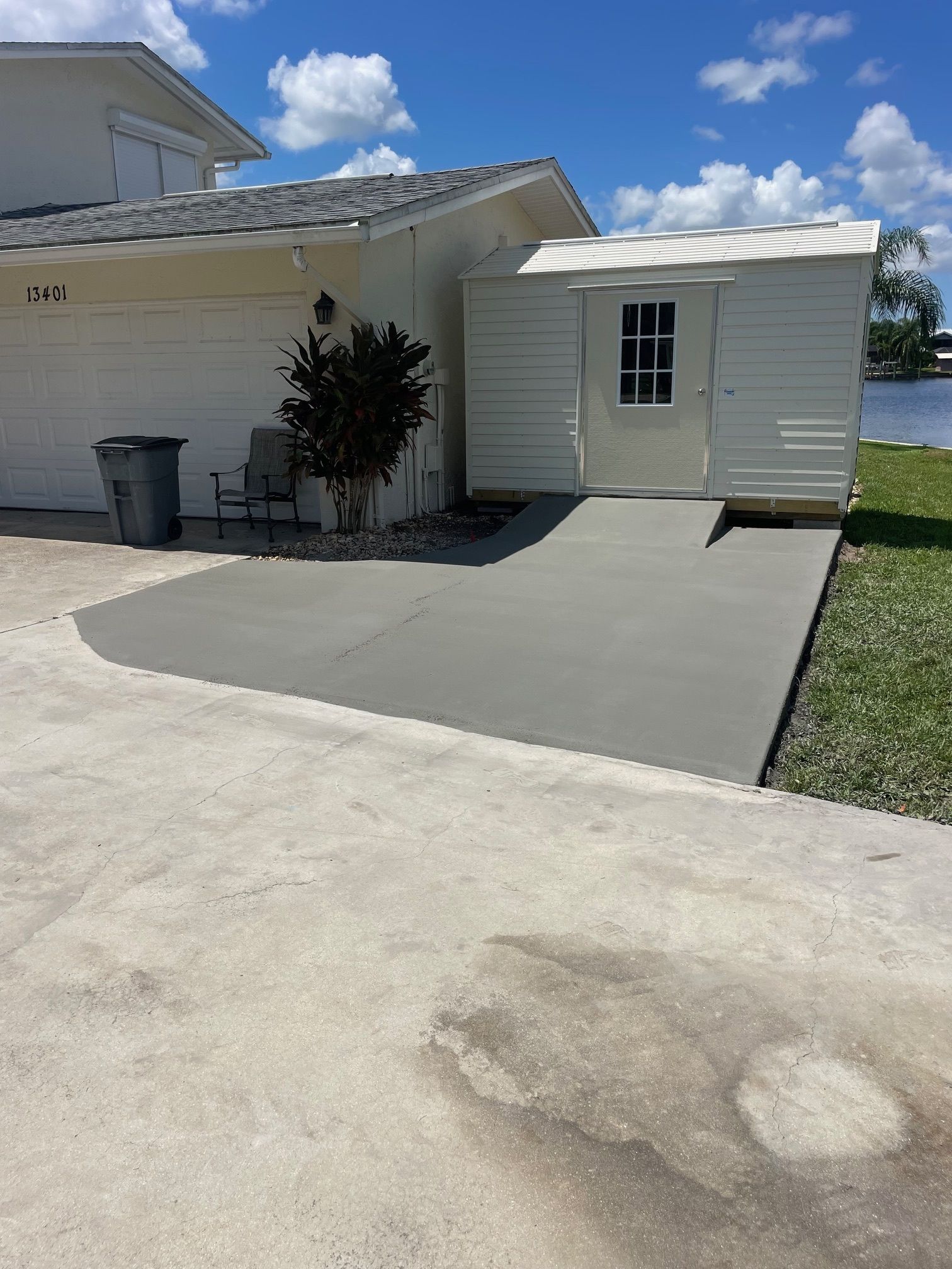 A concrete ramp leads to a shed beside a light-colored house. The ramp and shed are painted gray.