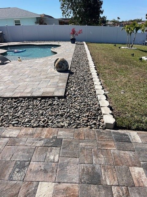 Backyard with pool, stone patio, rock border, and grass lawn.
