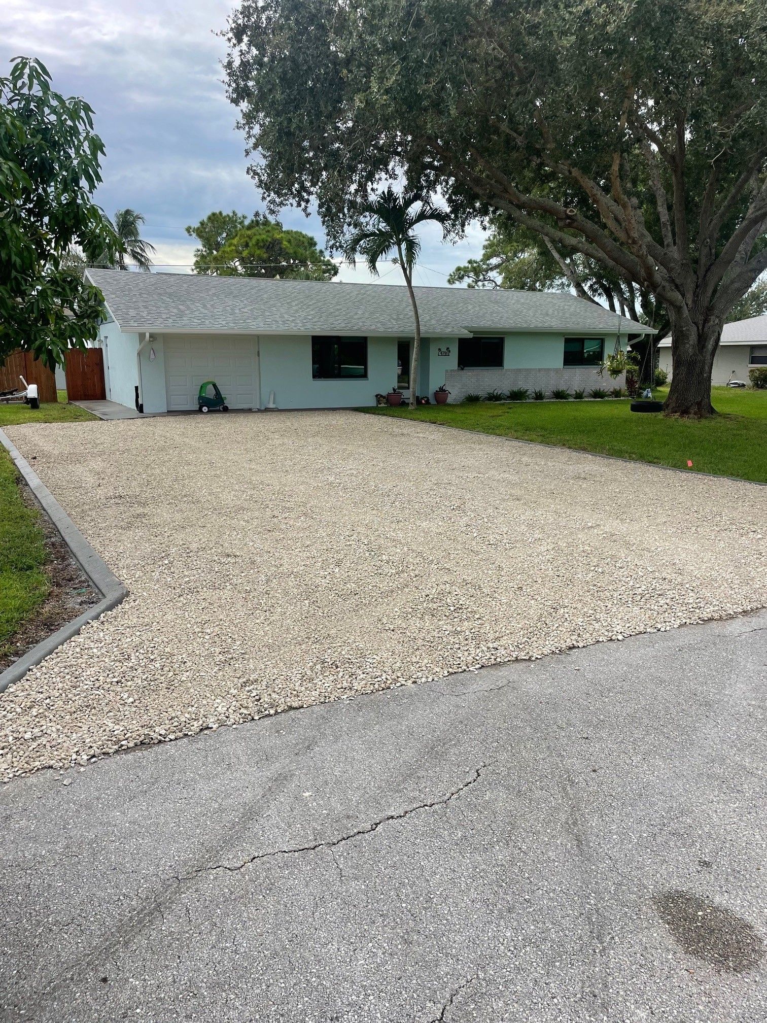 Light blue house with white gravel driveway, green lawn, and large tree.