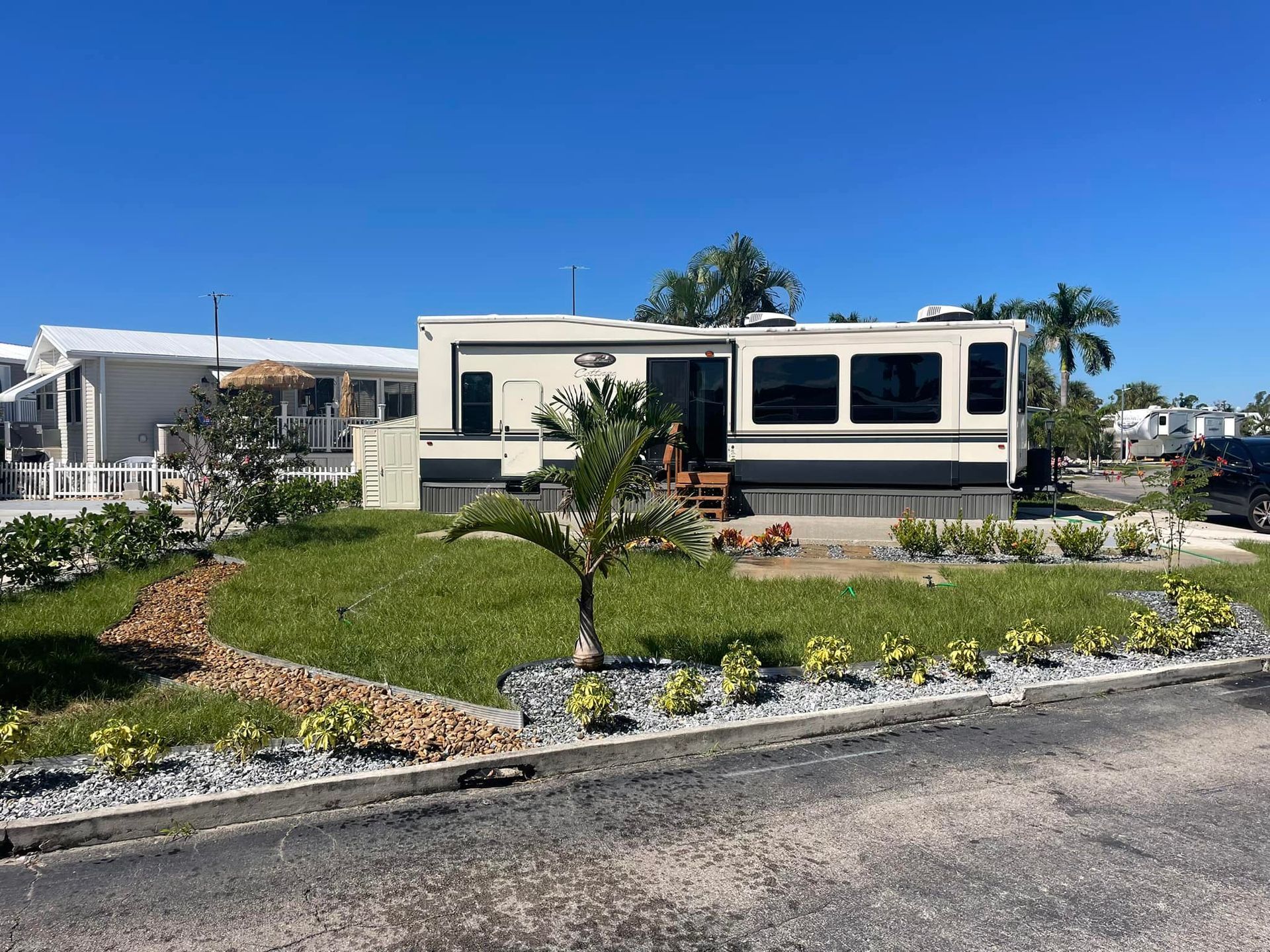 RV parked on a well-manicured lawn with landscaping; clear, sunny day.