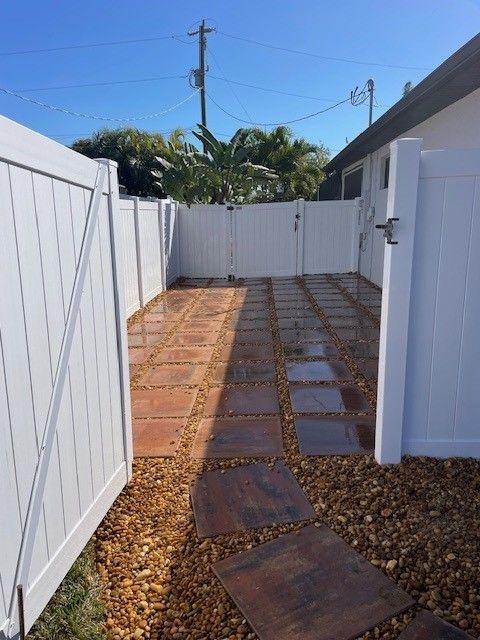 A fenced-in backyard patio featuring large, dark, square stone pavers surrounded by brown gravel.