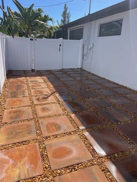 A courtyard with square stone pavers set in gravel, partially washed clean, showing a contrast between dirty and clean areas.