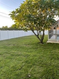 Lush green lawn, white fence, and a tree in front of a house with a screened porch.