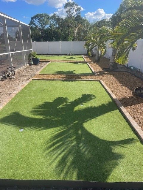 A backyard putting green with artificial turf, palm tree shadows, and wooden borders.