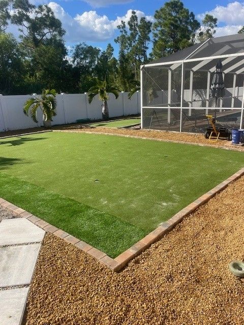 A rectangular artificial lawn bordered by pavers and gravel, next to a screened porch.