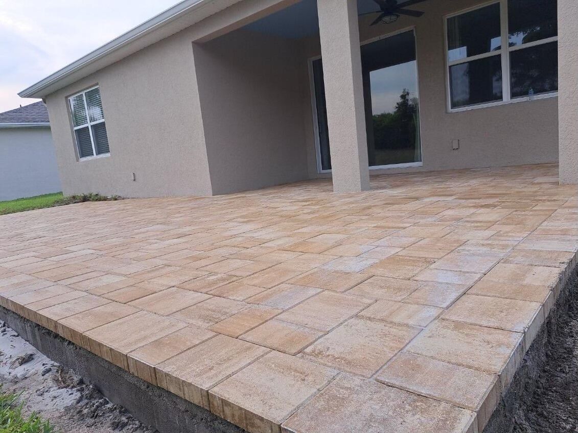 A brick patio with a beige house in the background.