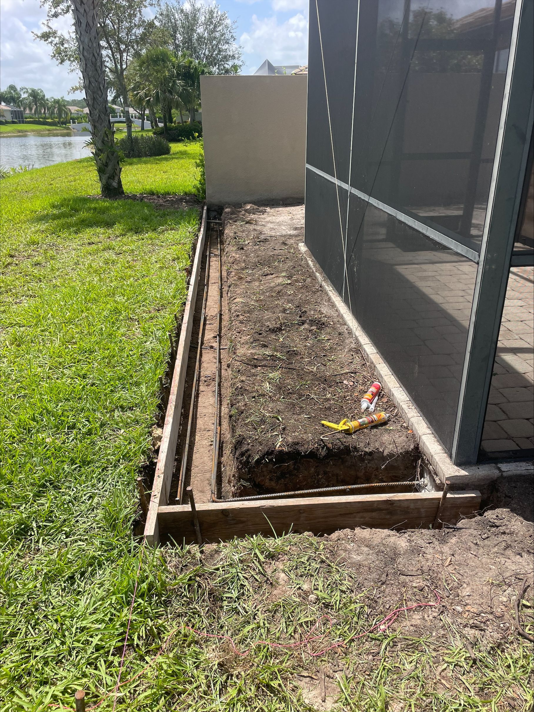 A rectangular dirt bed between a screen patio and wall, framed by concrete with grass on the left.