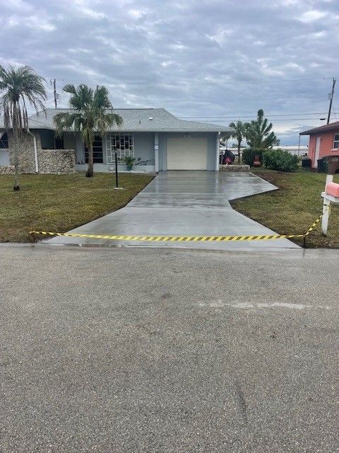 House with freshly poured gray concrete driveway; yellow tape blocks entrance.