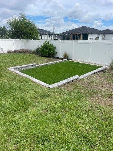 A square patch of green artificial turf surrounded by a concrete border in a backyard.
