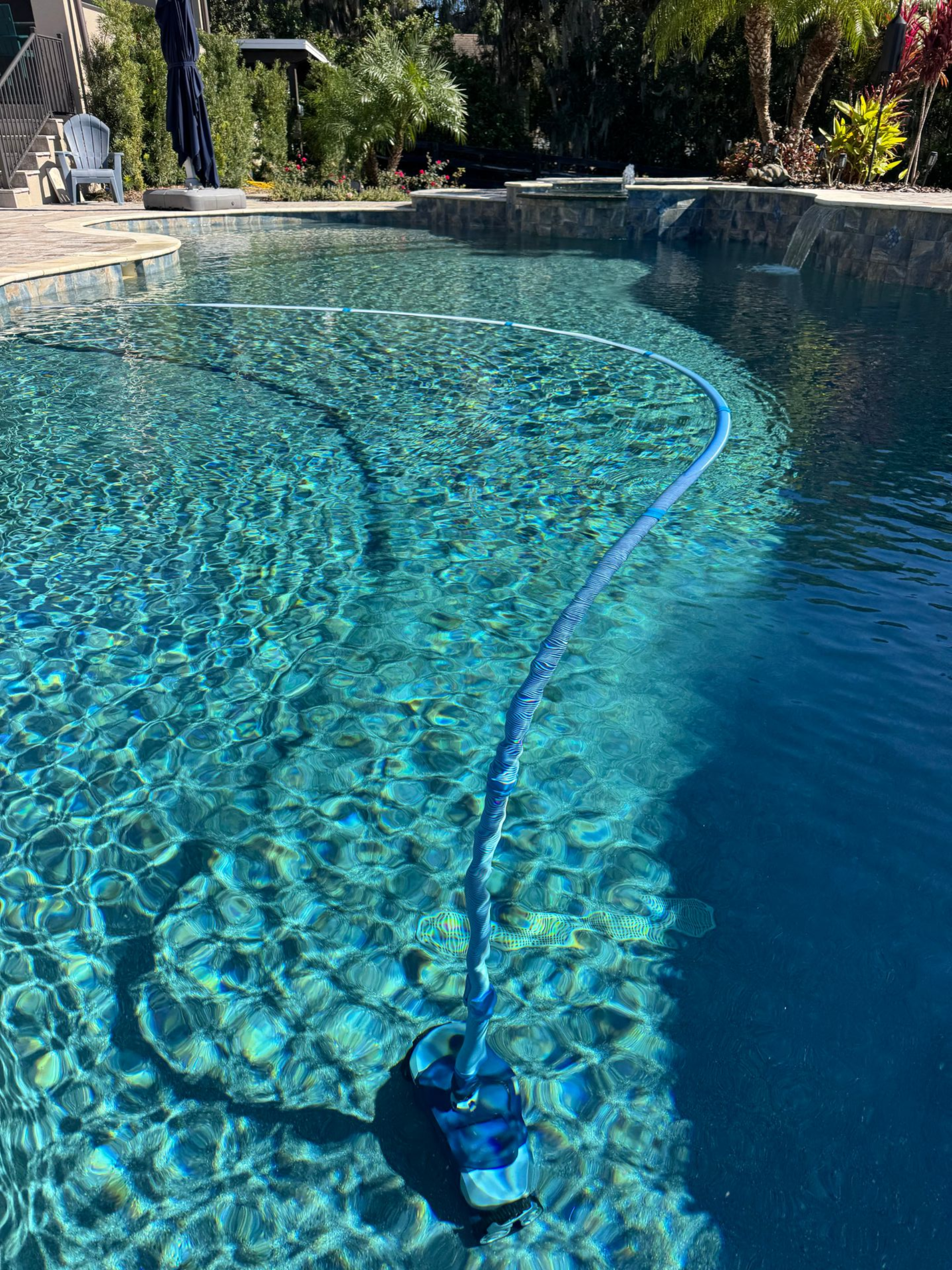 Pool cleaner scrubbing a clear, turquoise pool on a sunny day.