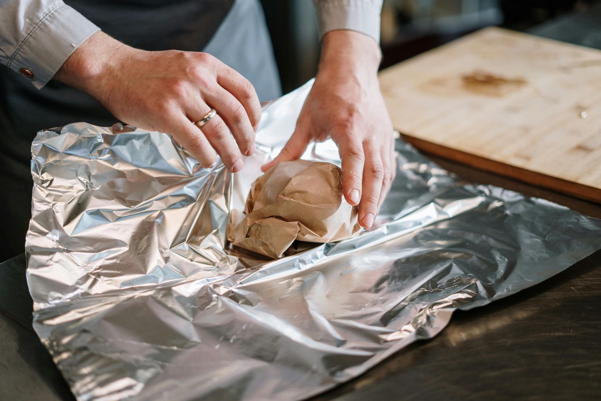 A person is wrapping a piece of meat in tin foil.