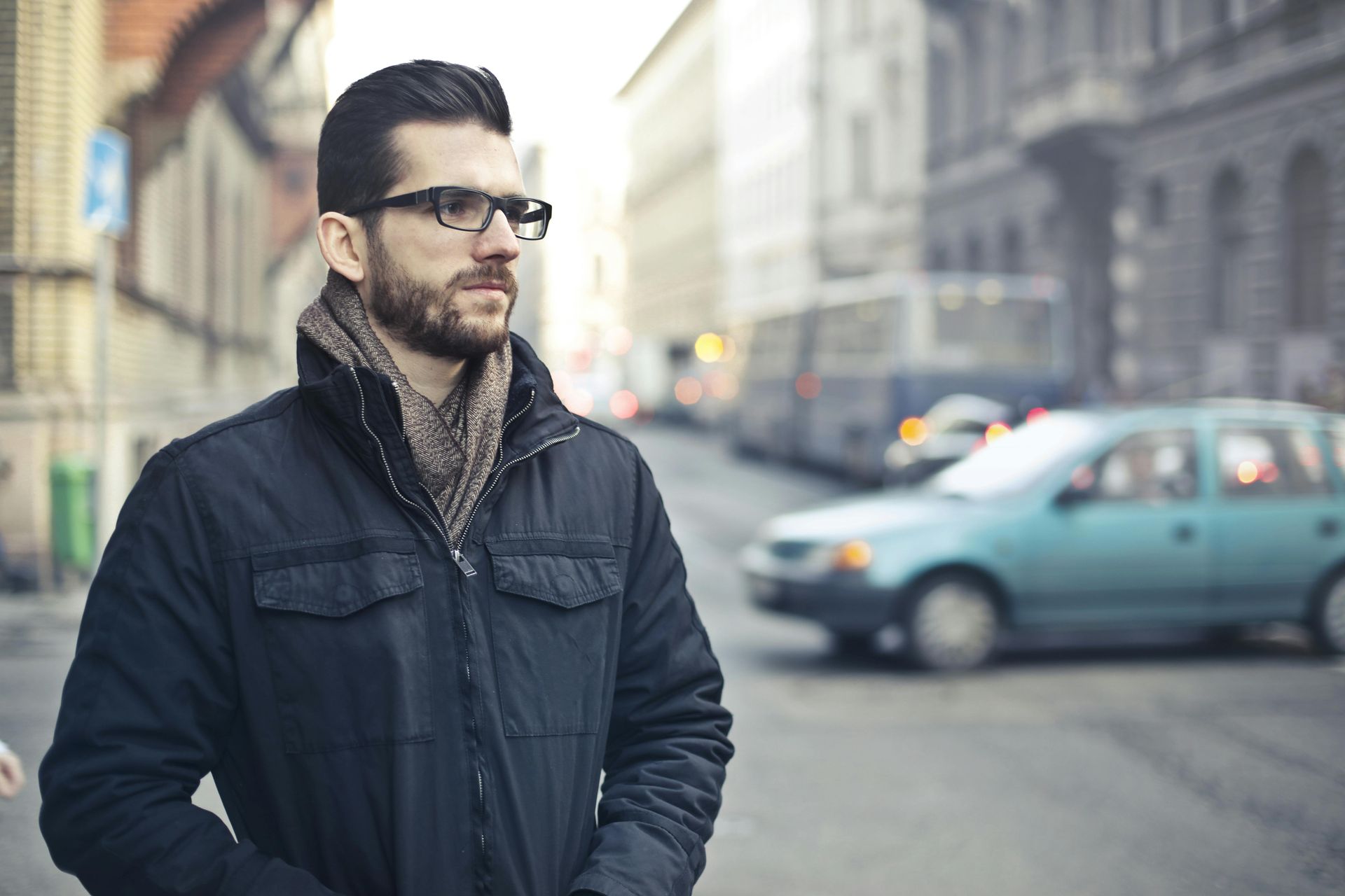 A man wearing glasses and a scarf is standing on a city street.