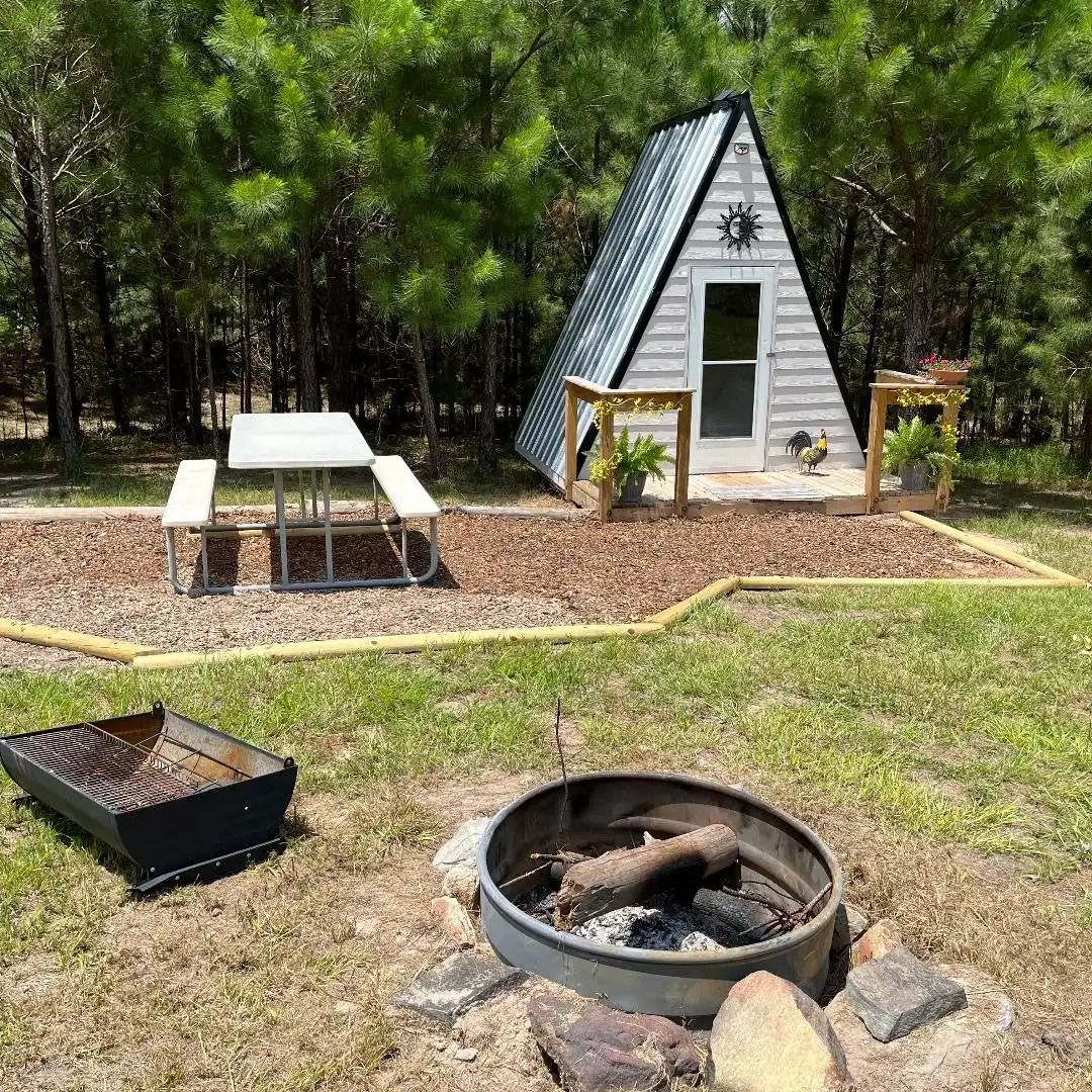 A-frame cabin, picnic table, and fire pit in a wooded campground.