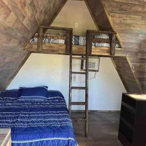 Loft bedroom with a blue bed, wooden ladder, and small loft bed under a slanted ceiling.