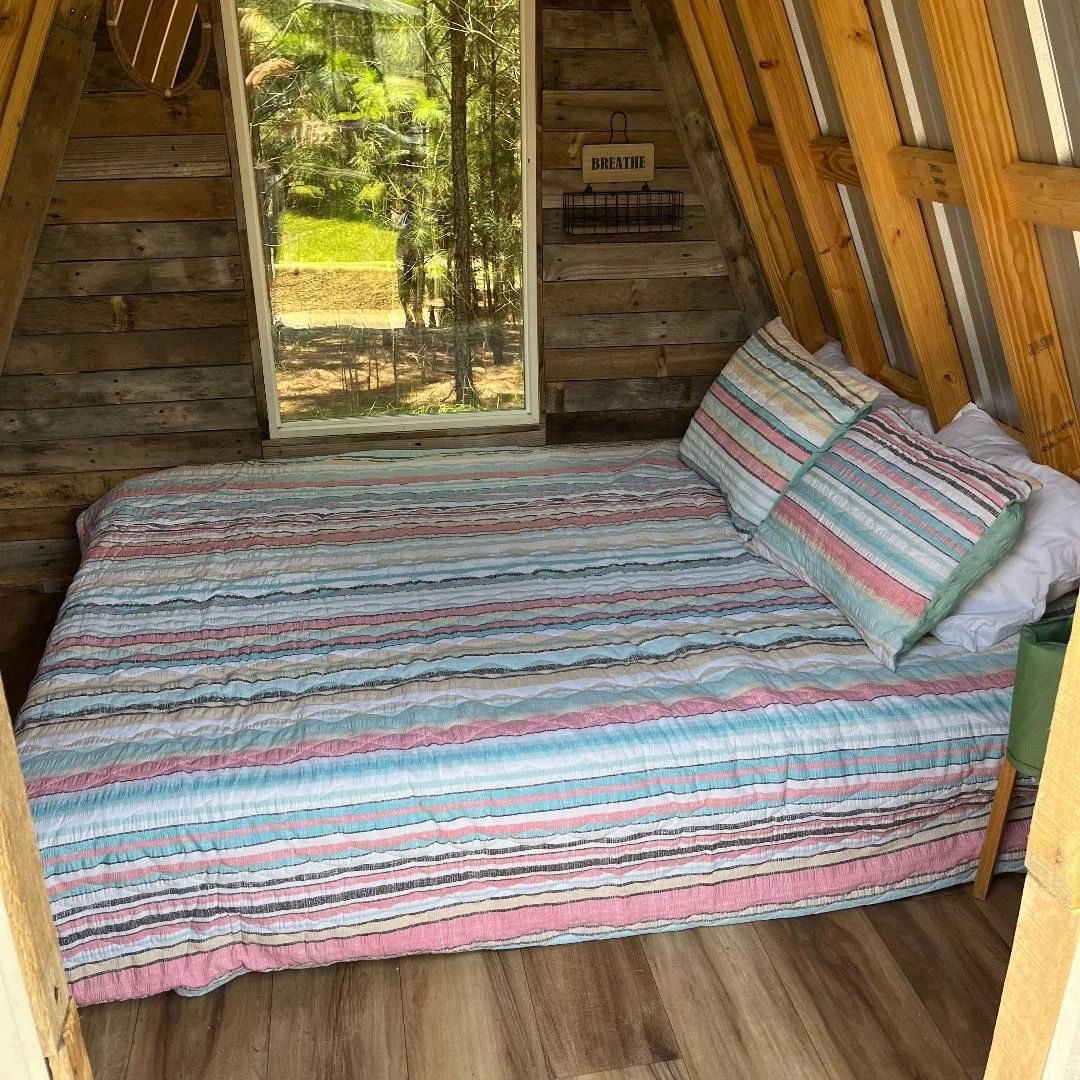 Cozy wood cabin bedroom with a striped bedspread, pillow, and a window looking out to trees.